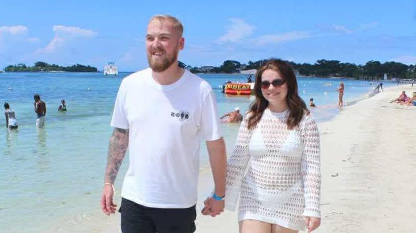 A smiling man and woman hold hands on a sandy beach