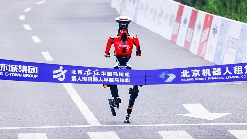 Robot a chorff coch a coesau du yn cyrraedd diwedd hanner marathon yn China yn gynharach eleni. Y tu ol i'r robot mae'r hewl yn glir. Ar y tap sy'n nodi diwedd y ras mae ysgrifen mewn sgript Chineaidd ar ruban las.