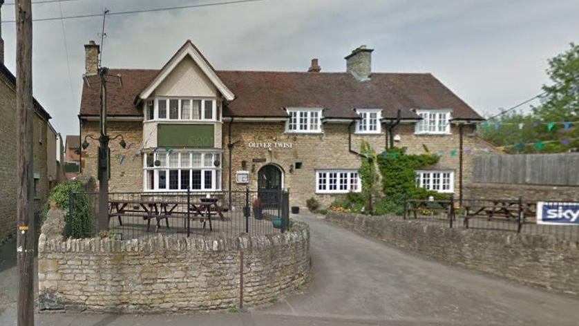 Two-storey pub building with bay window on both floors to the left and smaller windows to the right. There is a driveway to the entrance between two stone walls. "Oliver Twist" is spelt out in a sign above the door.