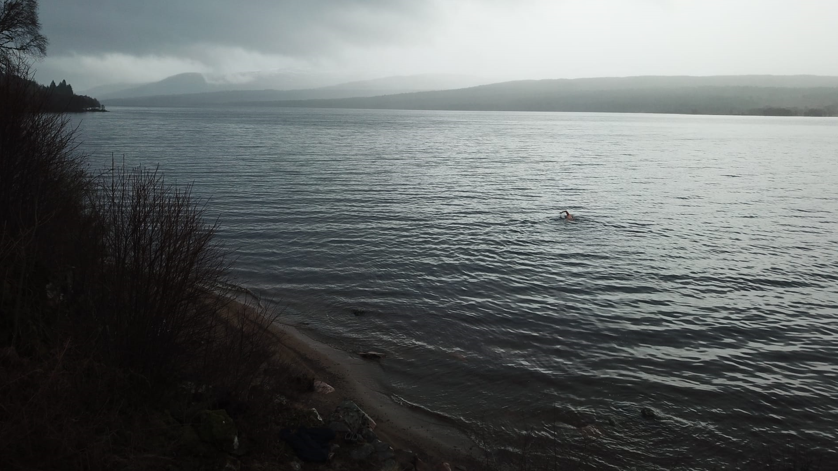 Someone swimming in open water with a murky backdrop of a mountainous region 