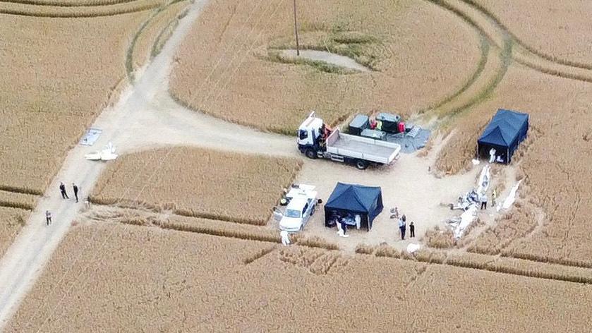 A drone image of investigators at the scene of the crash. A white plane can be seen badly damaged and there are several tents set up around it. It is all based in a large field.