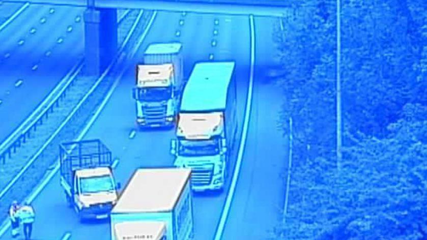 View from a motorway bridge showing lorries stopped and police officers standing on the carriageway