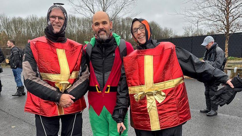 Three bikers in fancy dress - two are dressed as Christmas presents and the other is an elf