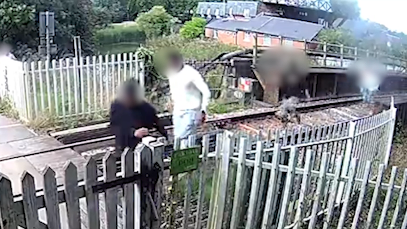 Four people running from right to left along a railway track. There is white fencing running either side of the tracks