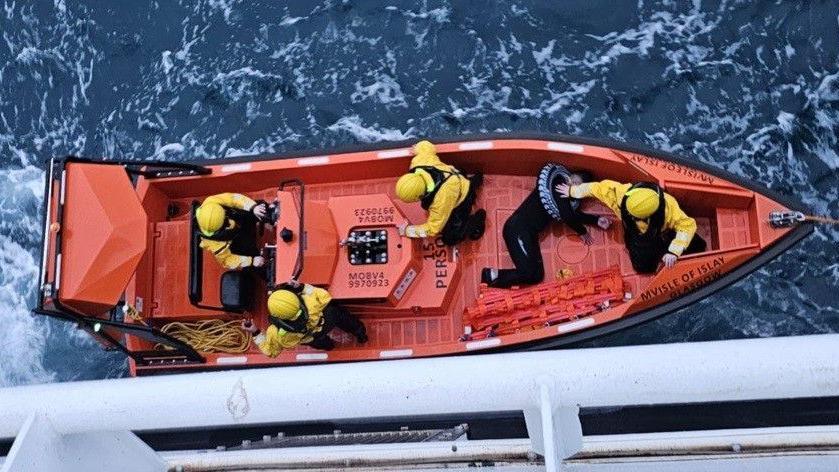 Sealladh air bàta-teasairginn ChalMac bho dheic an Isle of Islay a' coimhead sìos. Chìthear criutha ChalMac agus an duine air an do rinn iad cobhair.