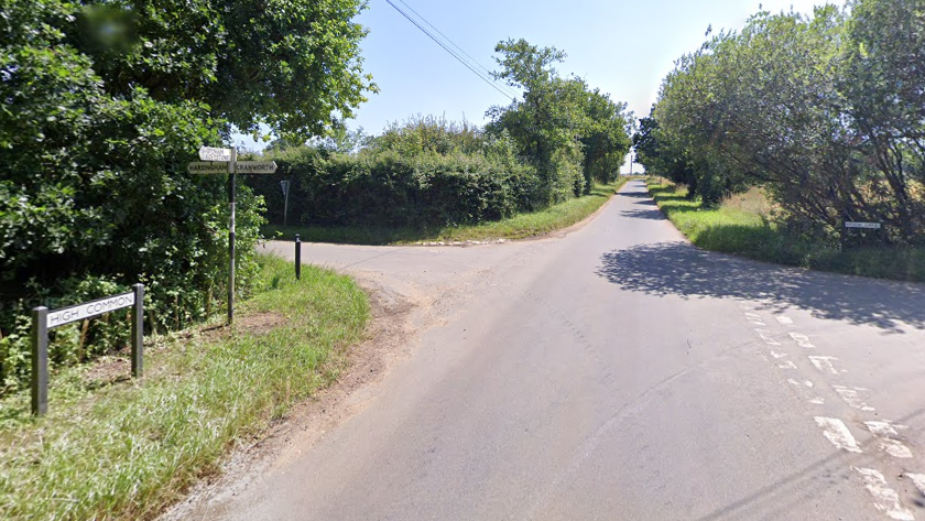 High Common in Cranworth. The road is at a junction with Hook Lane. There is a white road sign on the left which says HIGH COMMON. Next to it is a sign post directing motorists left to Hardingham and right to Cranworth. On the junction to the right is Hook Lane which has it's own road sign.