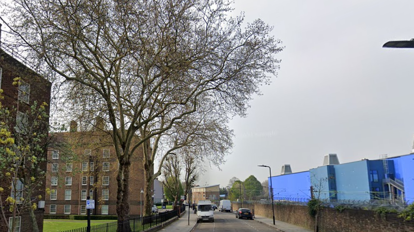 Google StreetView image showing art of Bodney Road. A period block of flats is visible on the left of the road, while a large blue industrial structure can be seen on the right