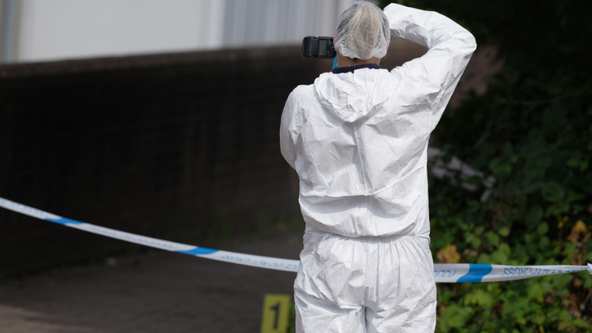 A person in a white hazmat suit taking a picture beyond police tape