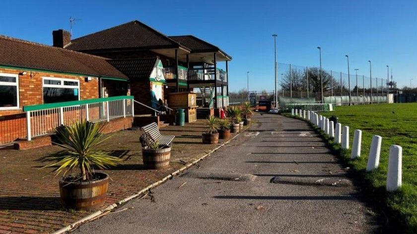 A pub seen from the outside next to a green field. The sky is blue and the sun is shining.