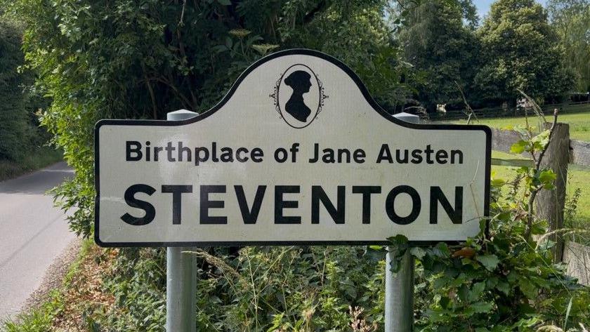 A road sign next to a country lane which reads "Steventon - Birthplace of Jane Austen"