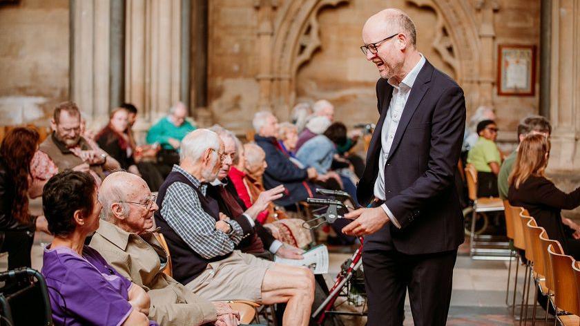 A man walking up to people in the audience during the Bristol Beacon event at Bristol Cathedral