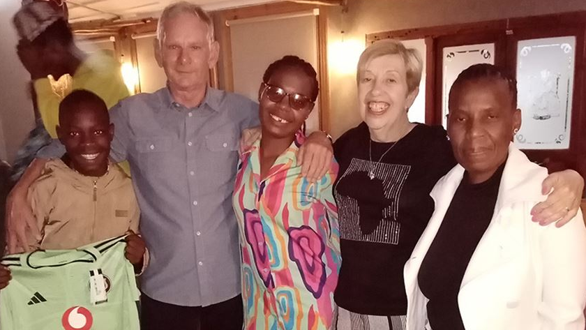 (From left to right) Choir member Muhle, Norman, Muhle's mum Lwazilenkosi Philanathi, Bridget, and Muhle's grandma Zanele during a trip to South Africa. They're all standing next to one another with their arms over each other's shoulders in a line.