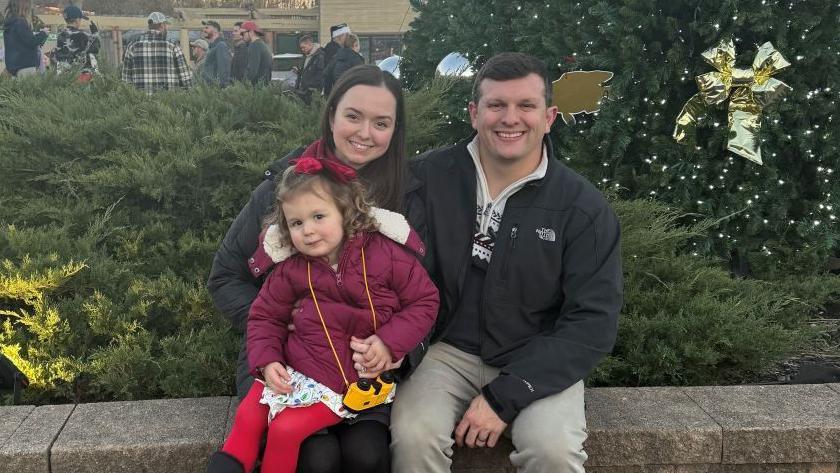 Amber Walliser and her husand and toddler smile at the camera wearing winter coats