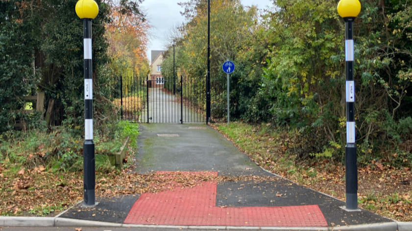 The crossing can be seen leading to the locked black gate with housing in view further on in the distance.