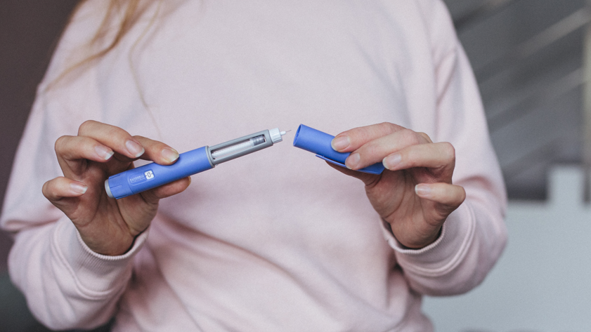 Person preparing a weight-loss injection. They have taken the lid off the blue pen to expose the needle.