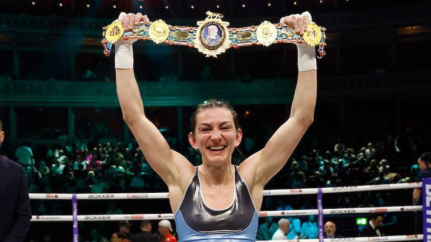 Karriss Artingstall holds the women's British featherweight title above her head after beating Raven Chapman