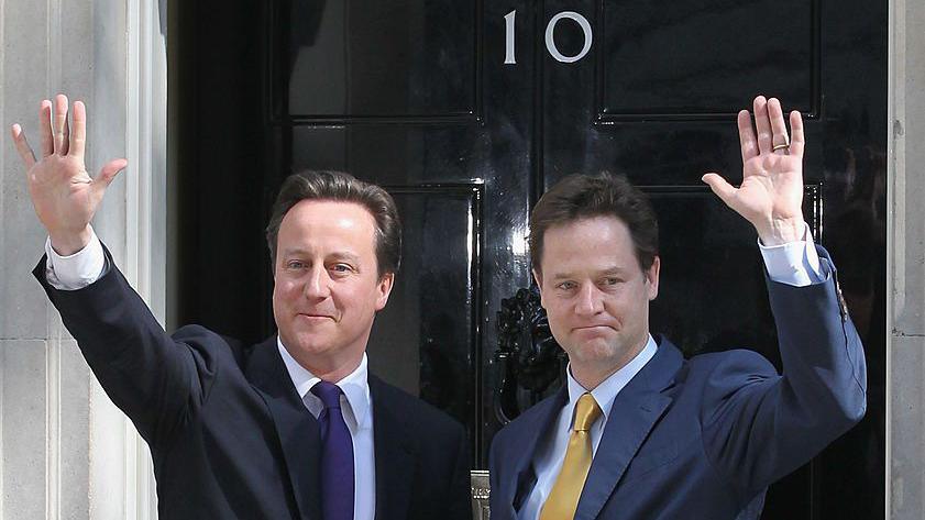 David Cameron and Nick Clegg wave outside the door of 10 Downing Street.