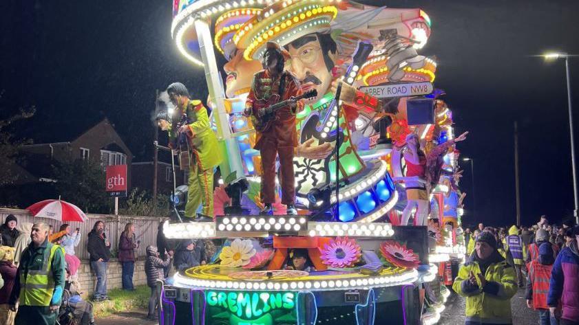 A bright coloured carnival cart with music legends performing on it. 