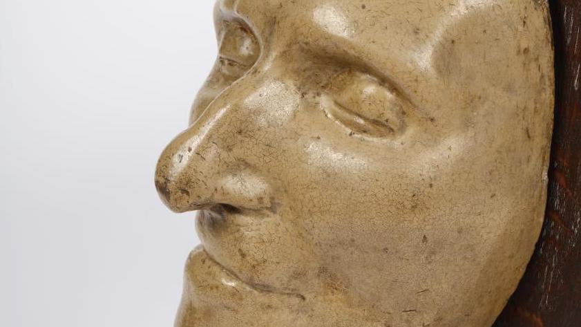 A mask made of yellowed plaster of Thomas Paine's face mounted on dark wood.