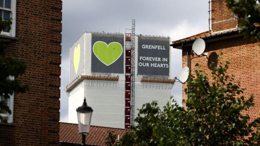 Grenfell Tower after the fire, covered with sheeting that has a big green heart and reads: "Grenfell - Forever in our hearts"