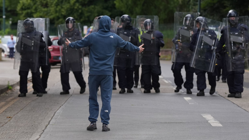 Man in hooded top with arms outstretched in front of a line of Irish riot police