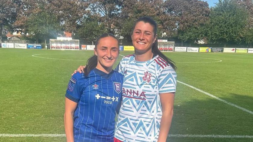 Sophie Peskett and Holly Turner, in opposing coloured kits, arm in arm on the pitch after their most recent league clash.