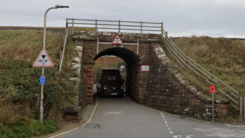 Streetview of a large black van coming through a single width tunnel below a railway line
