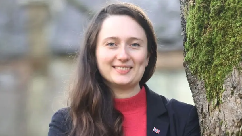 a smiling woman with long brown hair is wearing a black jacket and red top