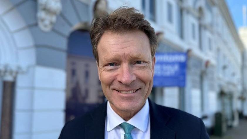 MP Richard Tice smiles as he stands in front of a row of units in Boston. He is wearing a blue tie, white shirt and black blazer.