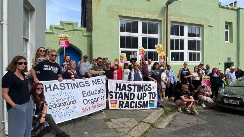 Male and female demonstrators carry placards outside Hastings Mosque on Sunday