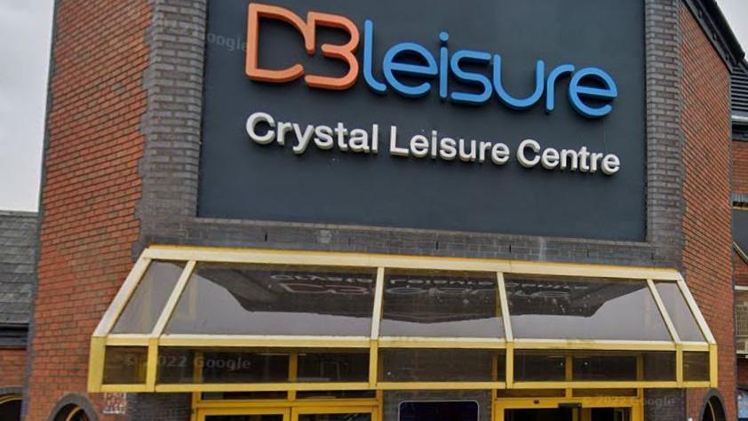 Red brick building with a grey sign that reads "DB LEISURE, Crystal leisure centre" in orange, blue and white text