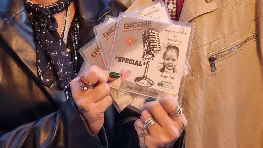 A close up of Mr and Mrs Champness holding four CD covers with Phoebe's black and white picture on it. 