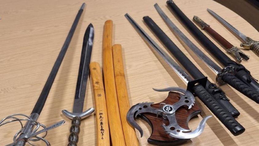 A table with a collection of bladed weapons, including swords, on it.