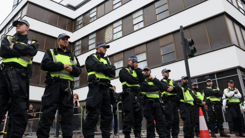 A row of police lined up on a street outside of a tall building 