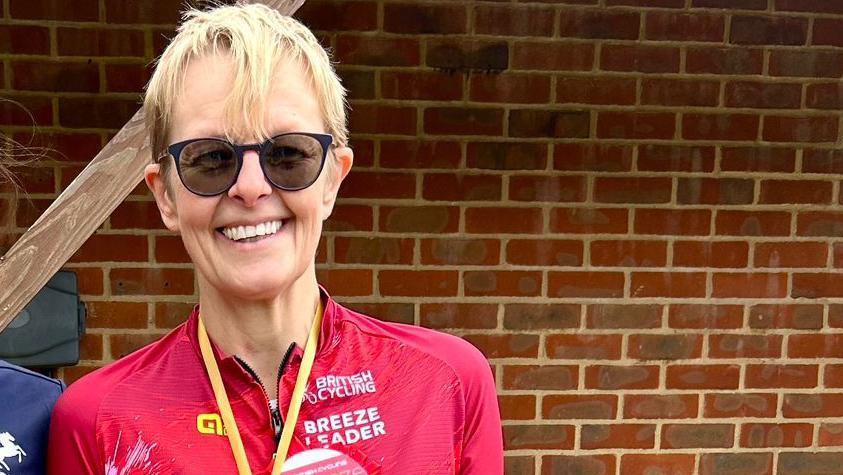 Vicky Smith  in a red cycling top in front of a brick wall