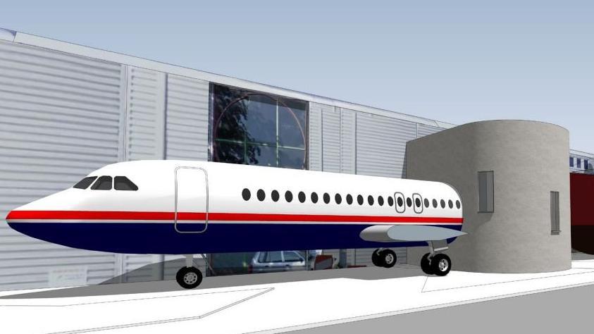 An artist's impression of half a plane attached to a museum. A two-storey building meets the plane near where its wing would be. Next to the plane is the museum.