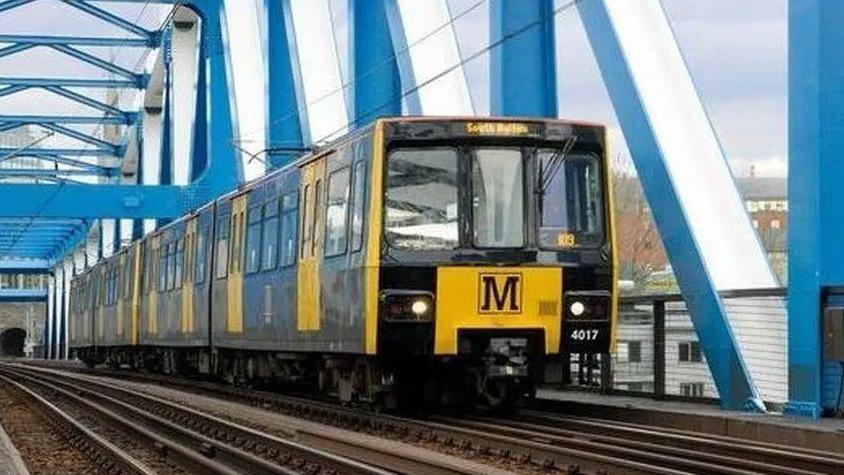 A Metro train with black and yellow livery on tracks on the blue Metro bridge running between Newcastle and Gateshead