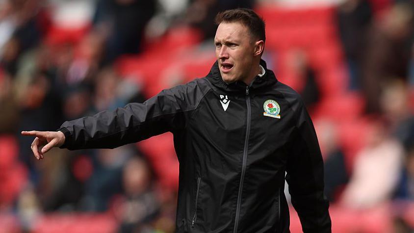 Phil Jones coaching from the sidelines at Stoke wearing a black Blackburn Rovers training top with the club badge of a red rose on it