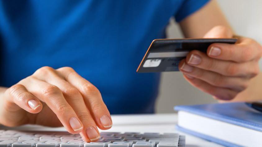 Library photo of one hand typing on to a keyboard and the other holding a credit card. 