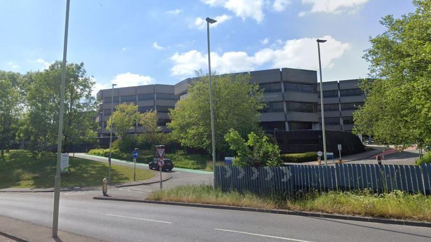 A Google street view image of a large office complex. Three octagonal buildings are visible, with alternating rows of concrete walls and windows.