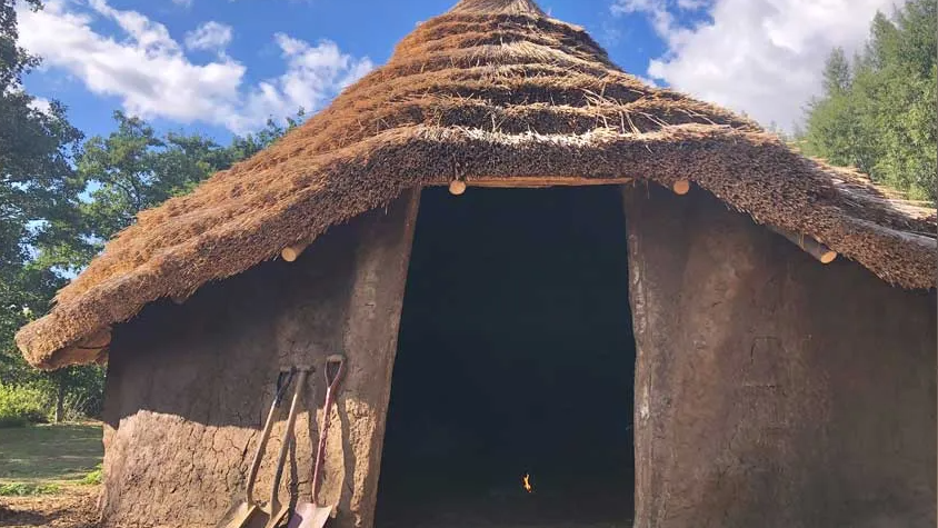 A roundhouse at Flag Fen Archaeology Park, there are three spades propped up outside.