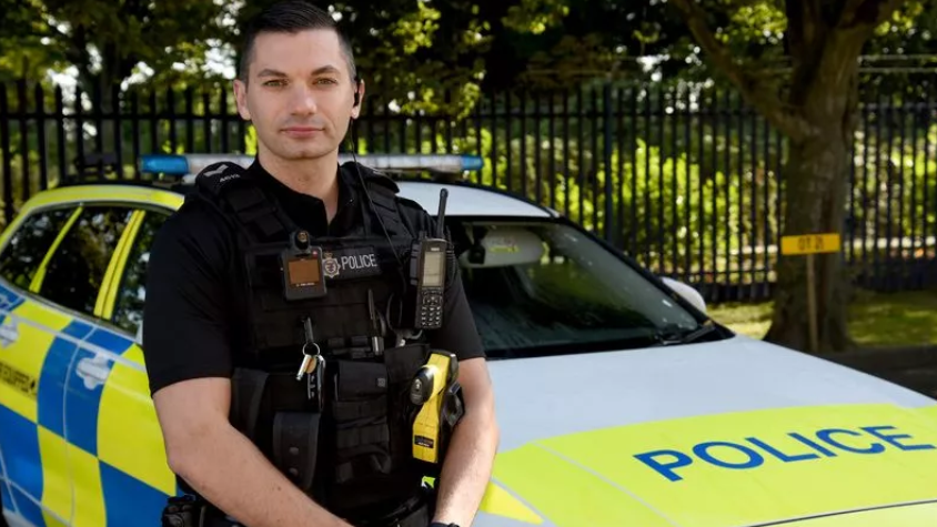 Sgt Luke O'Connell in police uniform standing in front of his marked police car