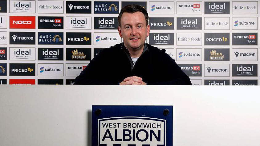 Dominic Price sits in his news conference above a club crest as he is introduced as West Bromwich Albion's new technical director
