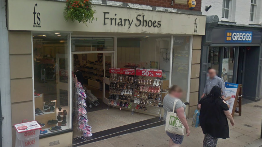 The shop has a beige sign and a light brown finish externally and shoe racks outside its entrance.