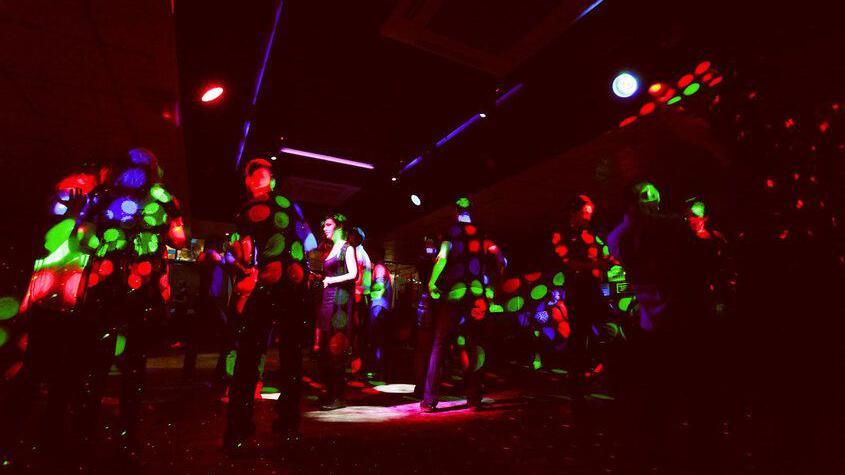 Dancers in a dark nightclub, with red, green and blue lights shining on them.