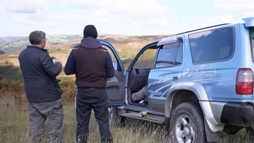 two men stand by a 4x4 overlooking a valley 