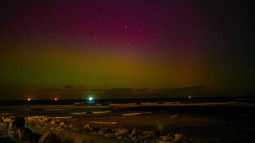 A dull yellow and pink sky above waves and a beach 