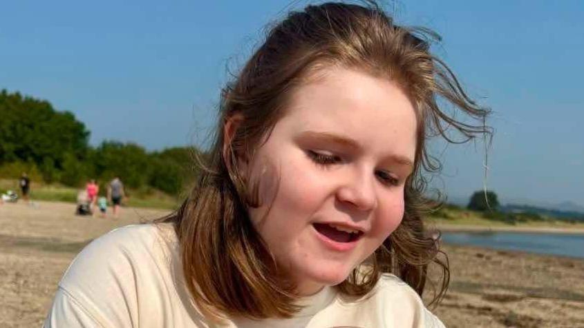 Anna smiles on a beach as her hair blows in the wind