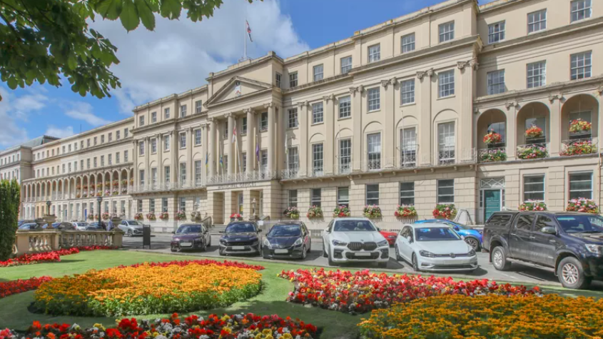 An exterior of the Regency Municipal Offices with floral displays in beds in the front and a row of parked cars