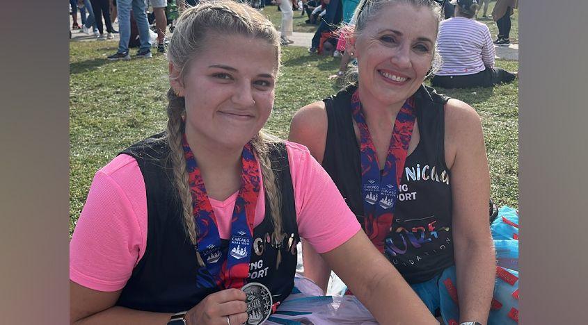 Sitting in a grassy area in Chicago are Gracie Nuttall - who has her long blonde hair in plaits - and her mum Nicola Nuttall, who has her blonde hair tied up. They are wearing marathon medals and are both smiling. Gracie is wearing a bright pink tutu while Nicola's is blue and red.